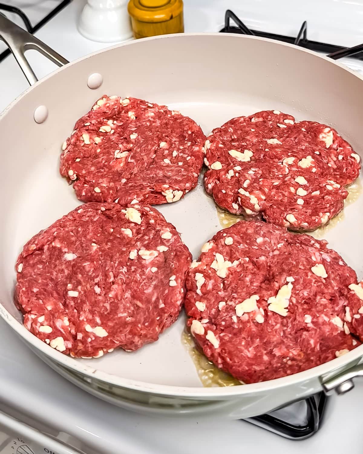 Four butter burger patties frying in a skillet.
