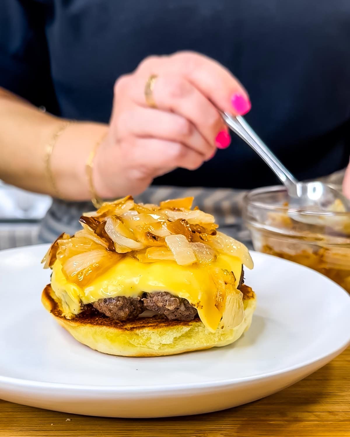 Spooning cooked onions on top of a butter burger.