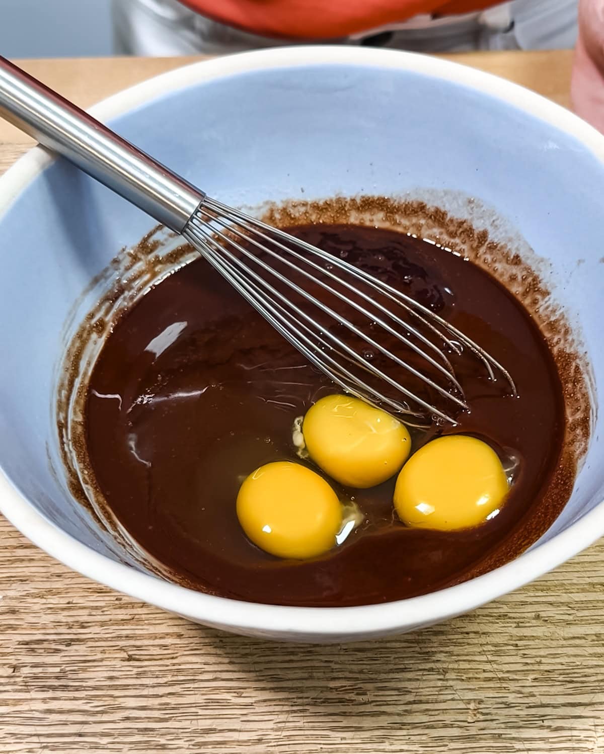Whisking in eggs and vanilla into a chocolate mixture. 