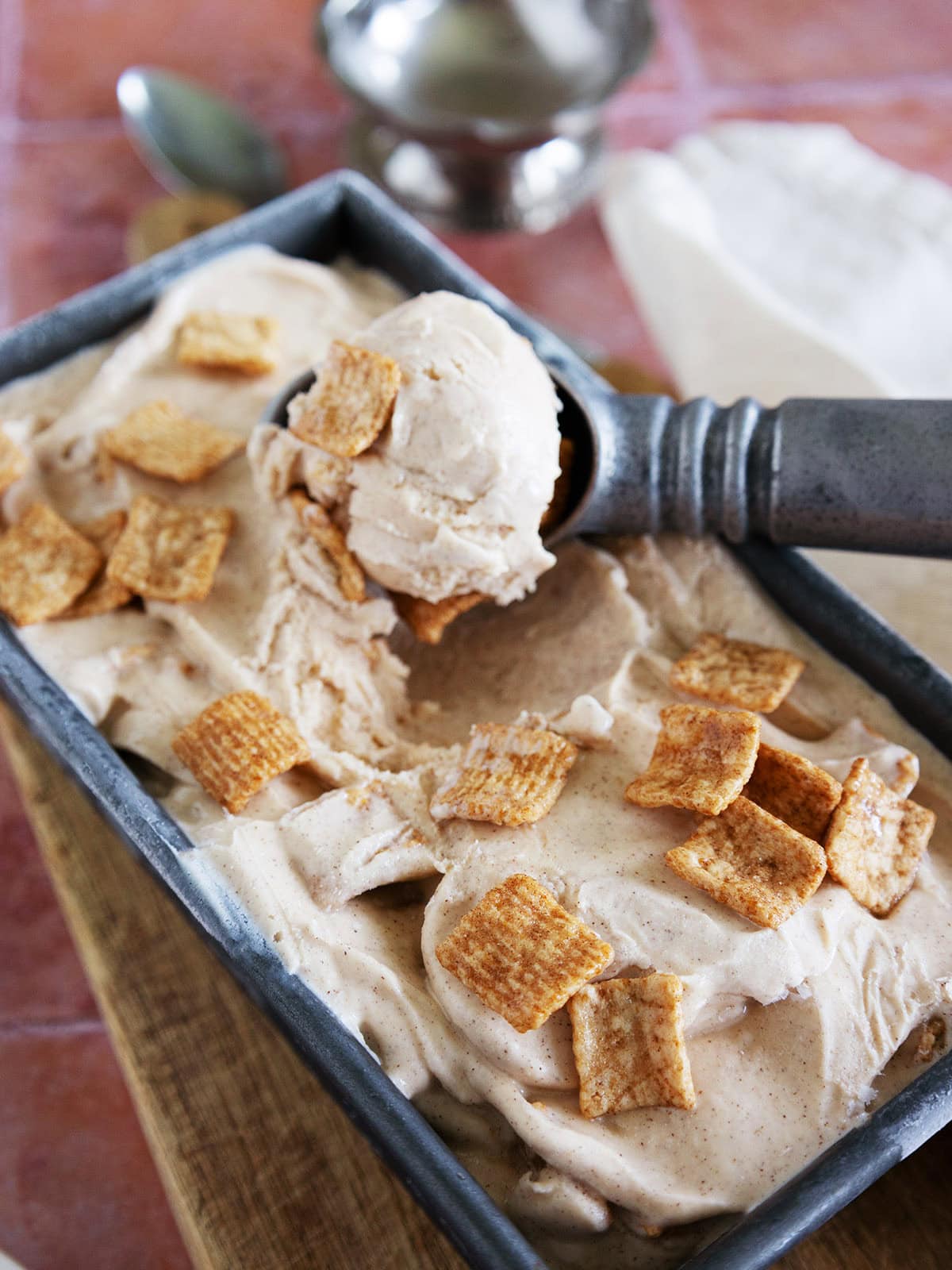 A pan of cinnamon toast crunch ice cream with a scooper scooping up ice cream.