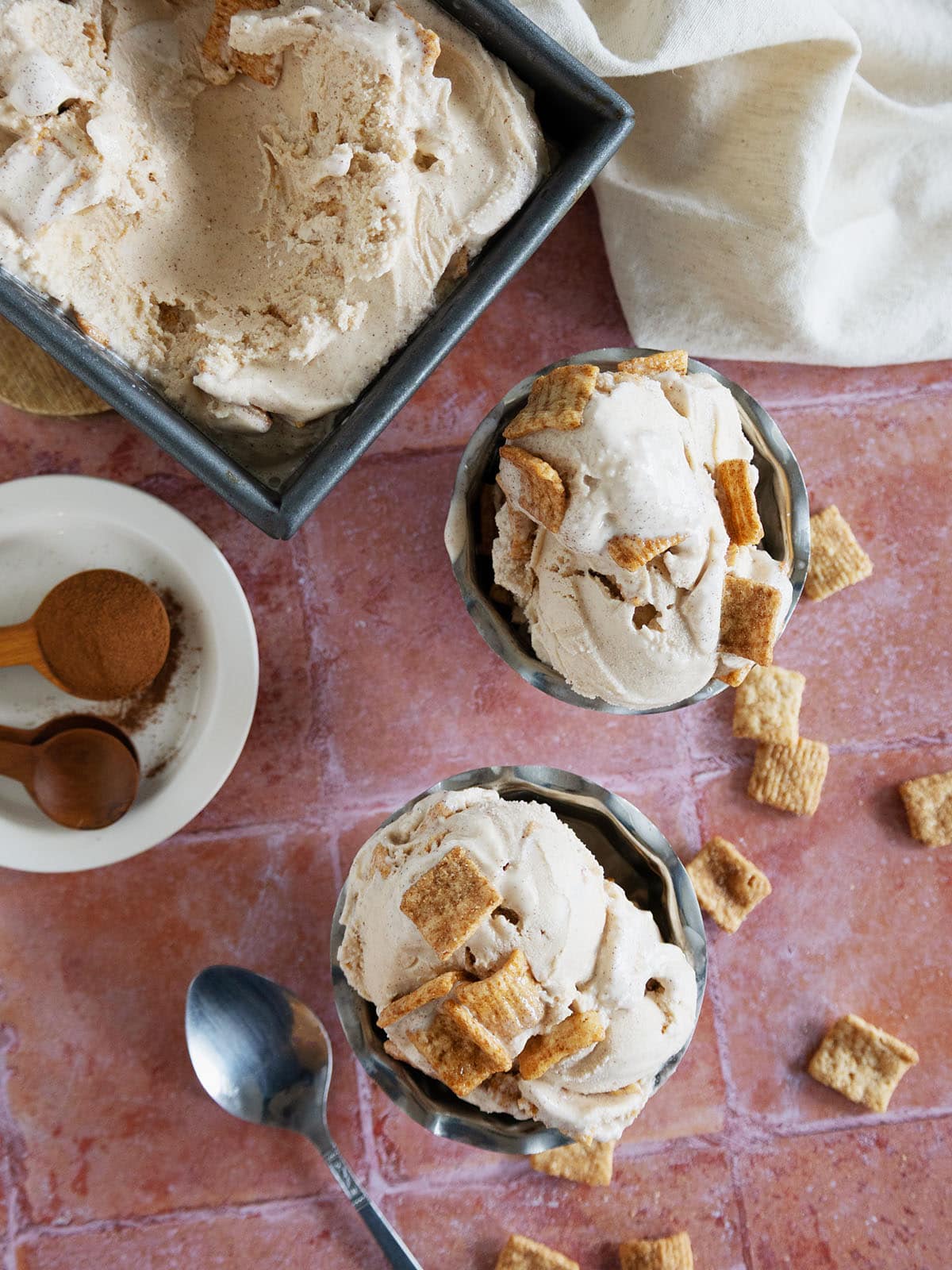 Top view of a loaf pan and two metal dessert bowls filled with cinnamon toast crunch ice cream.