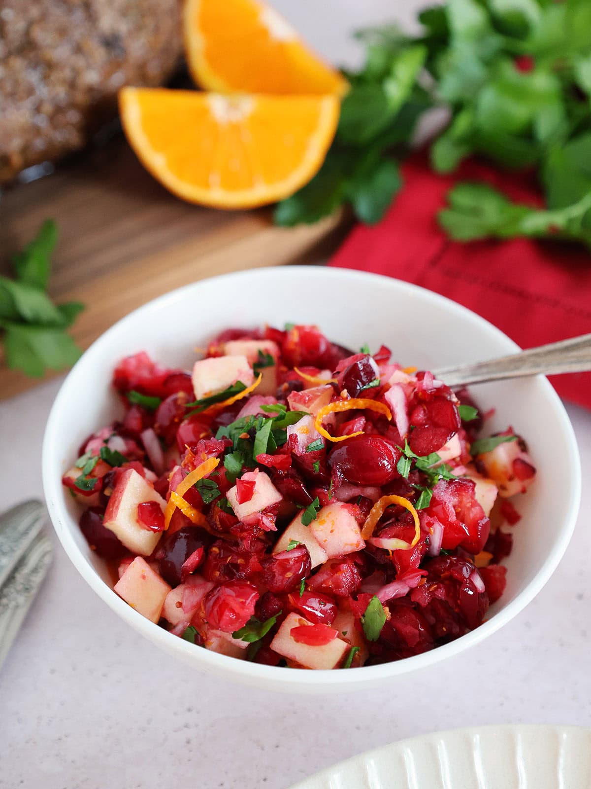 A bowl of cranberry relish with oranges and parsley in the background. 