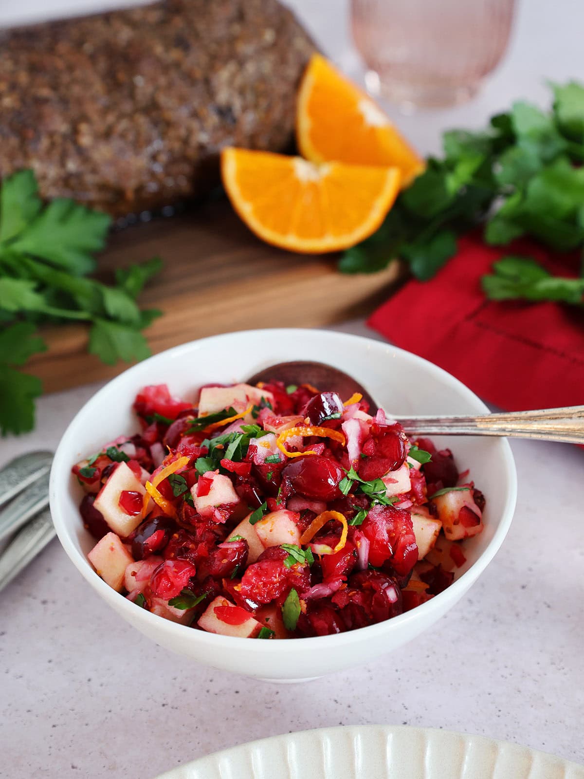 A bowl of cranberry relish with a tenderloin roast and oranges in the background.