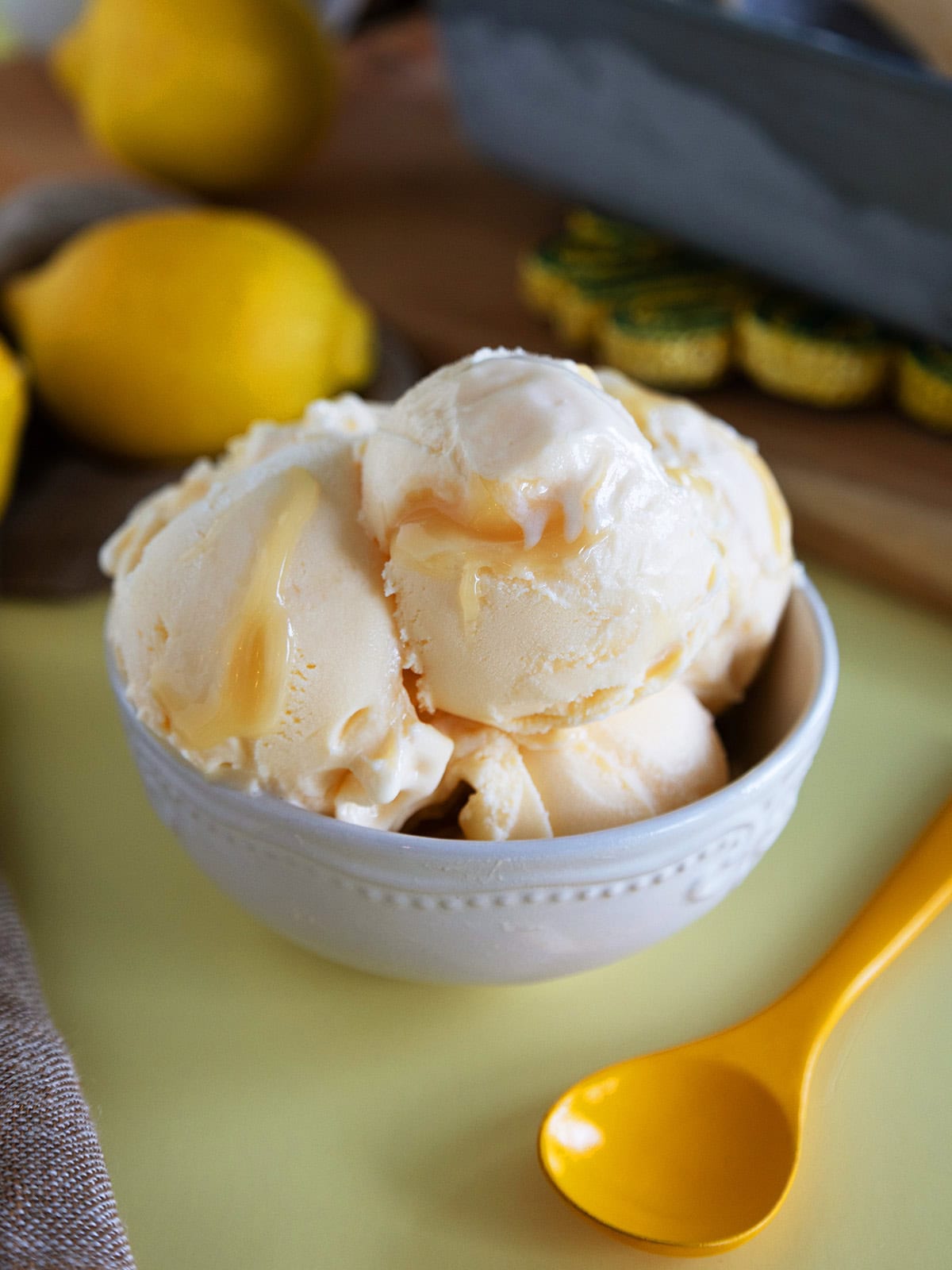 A bowl of lemon curd ice cream next to a yellow spoon.