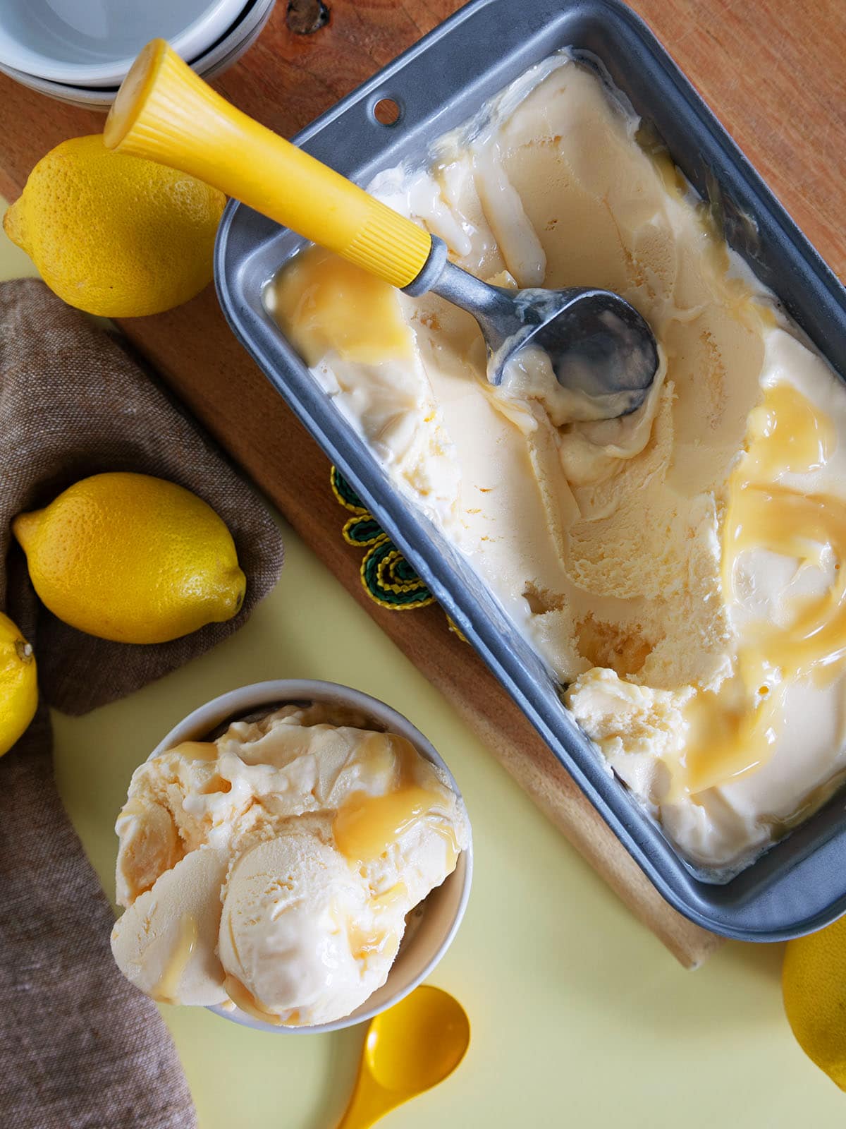 Top view of a pan of lemon curd ice cream next to a bowl filled with scoops of ice cream.