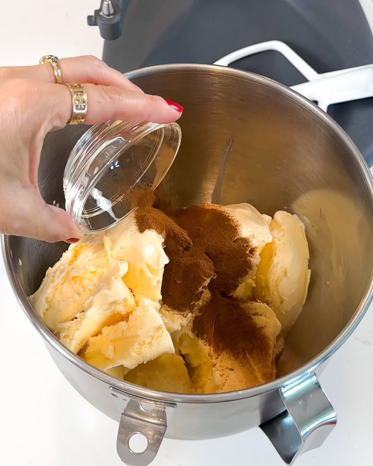 Pouring ground cinnamon into a mixing bowl of softened ice cream.