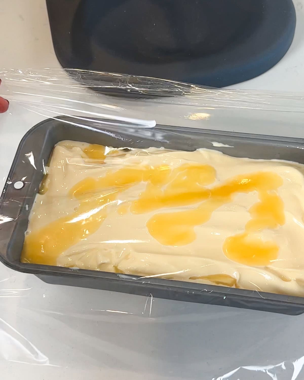 Placing plastic wrap over the top of lemon curd ice cream.