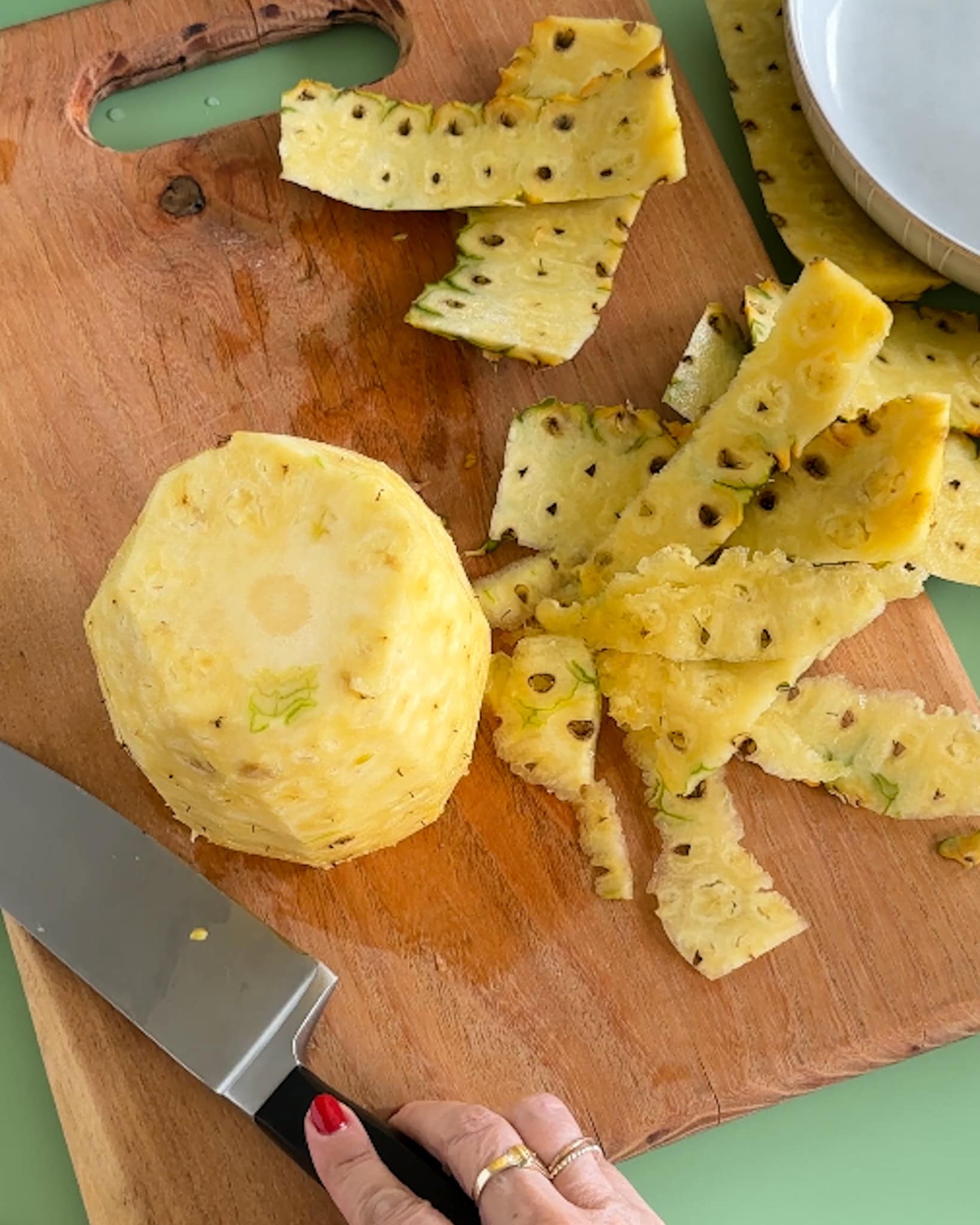 A peeled pineapple on a cutting board next to peel slices.