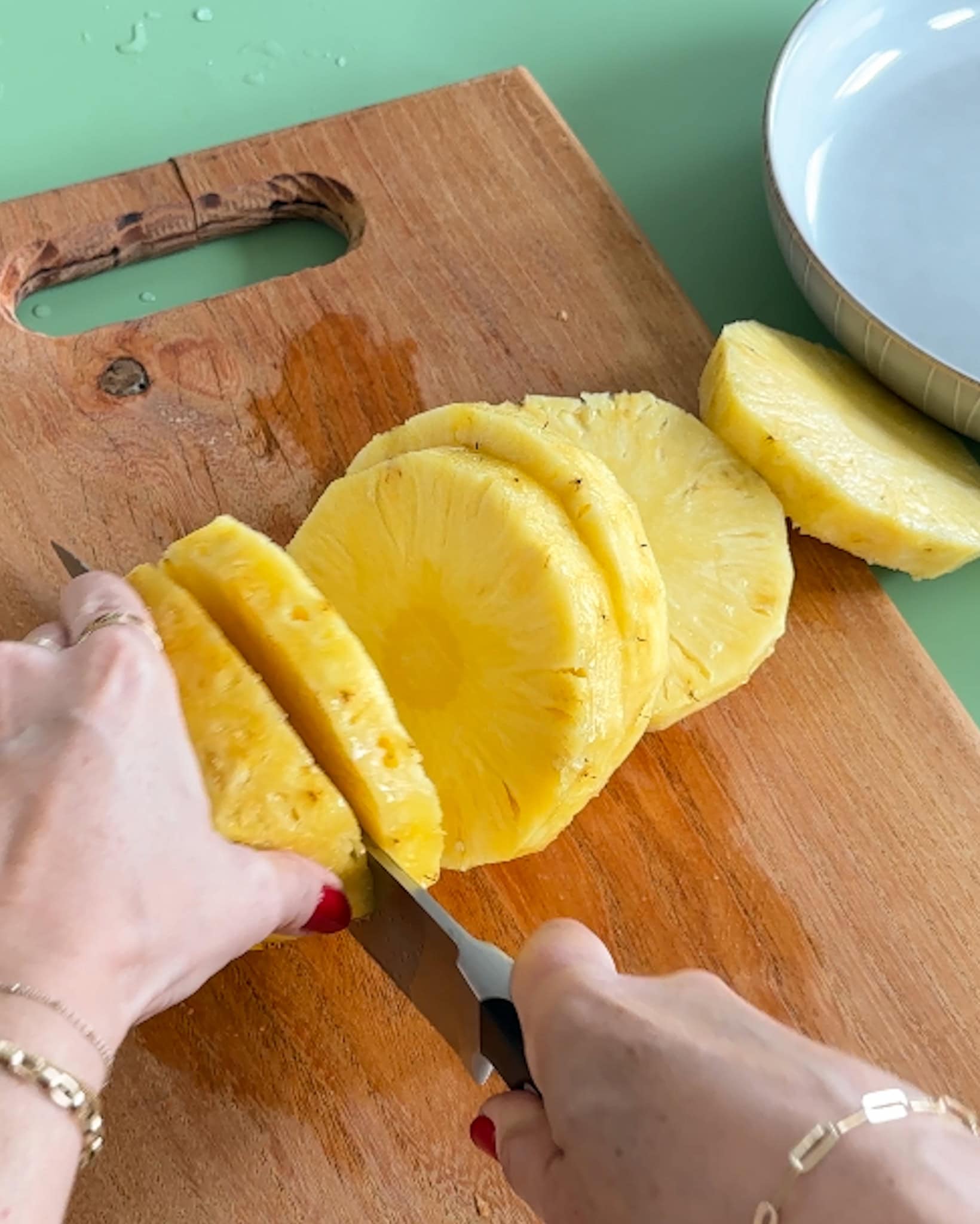 Using a knife to cut pineapple slices on a cutting board.