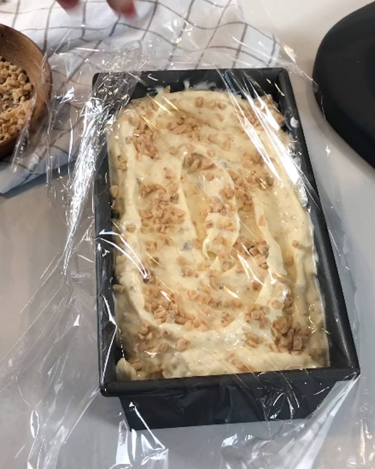 Plastic wrap being placed over the top of browned butter ice cream in a loaf pan.