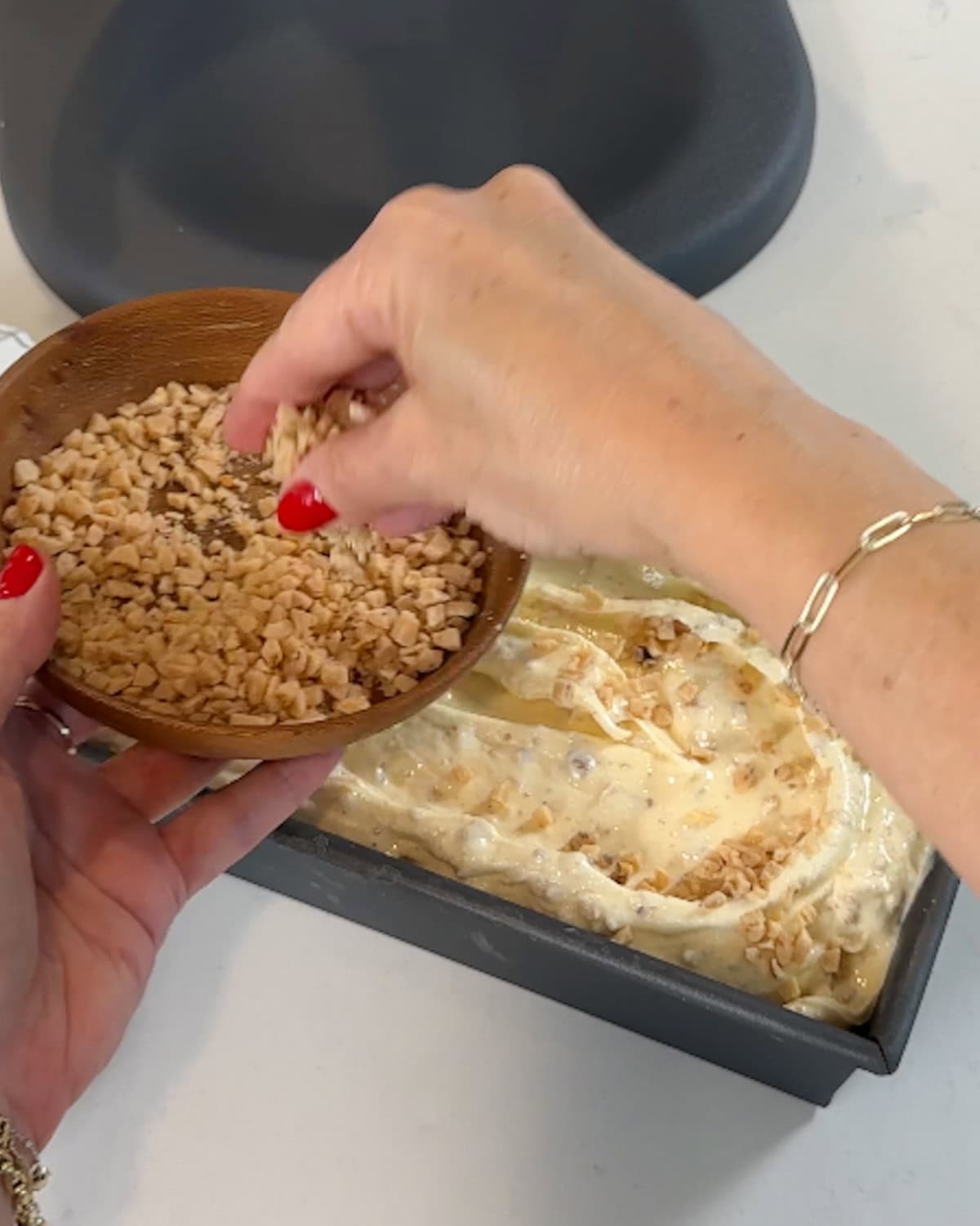 Sprinkling toffee on top of browned butter ice cream in a loaf pan.