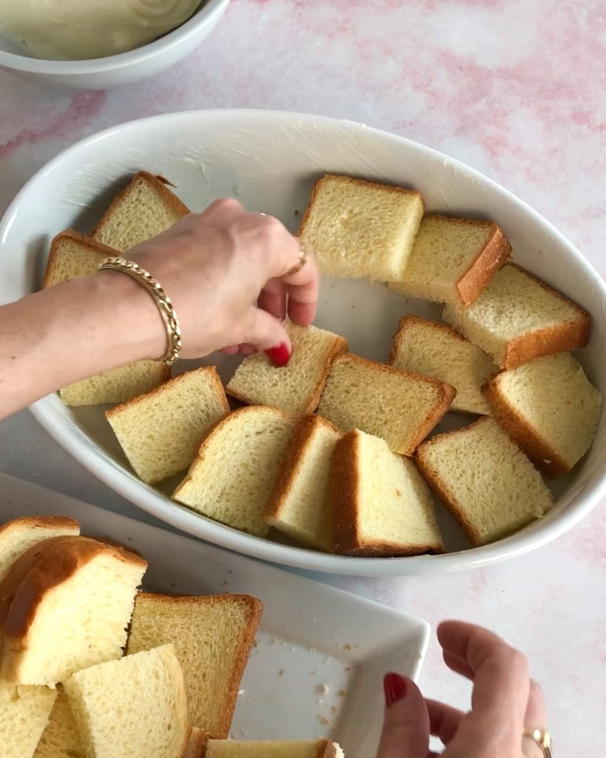A buttered baking dish with squares of brioche bread on the bottom for raspberry bread pudding