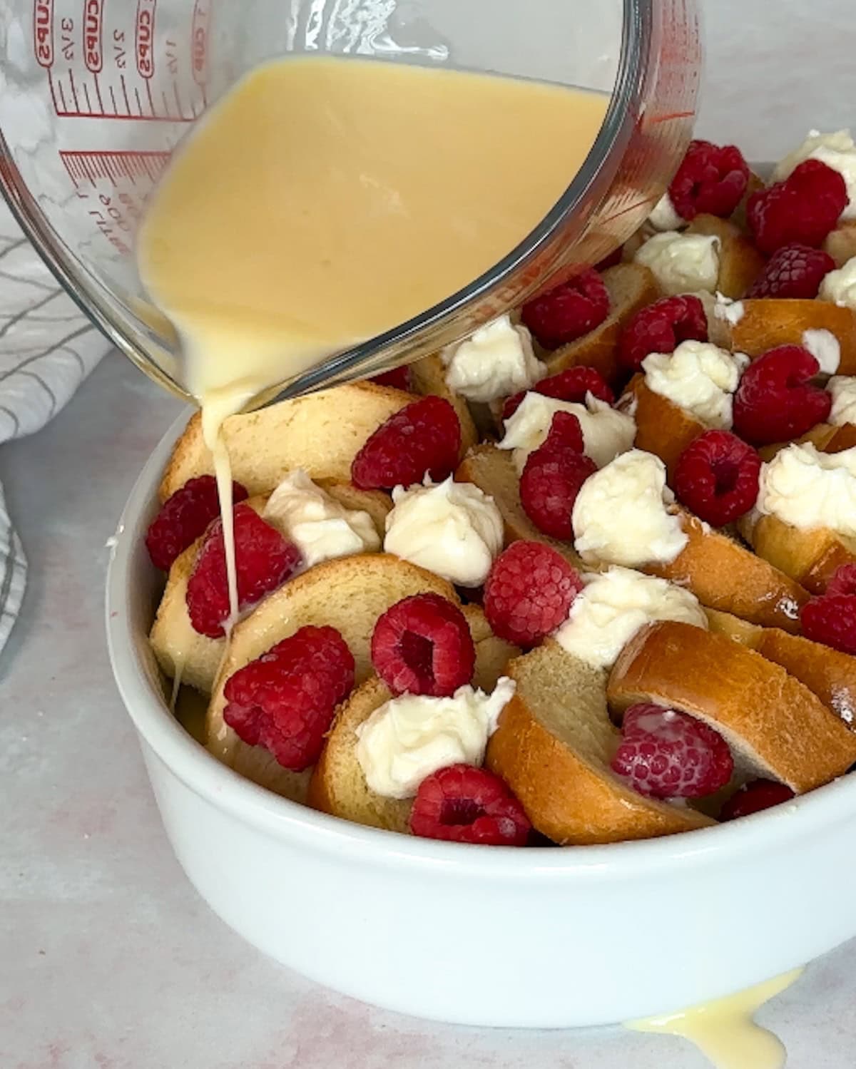 pouring custard mixture over raspberry french toast bake before cooking.