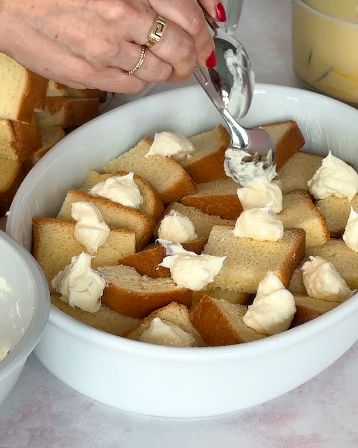 dolloping cream cheese mixture onto raspberry french toast in a dish.