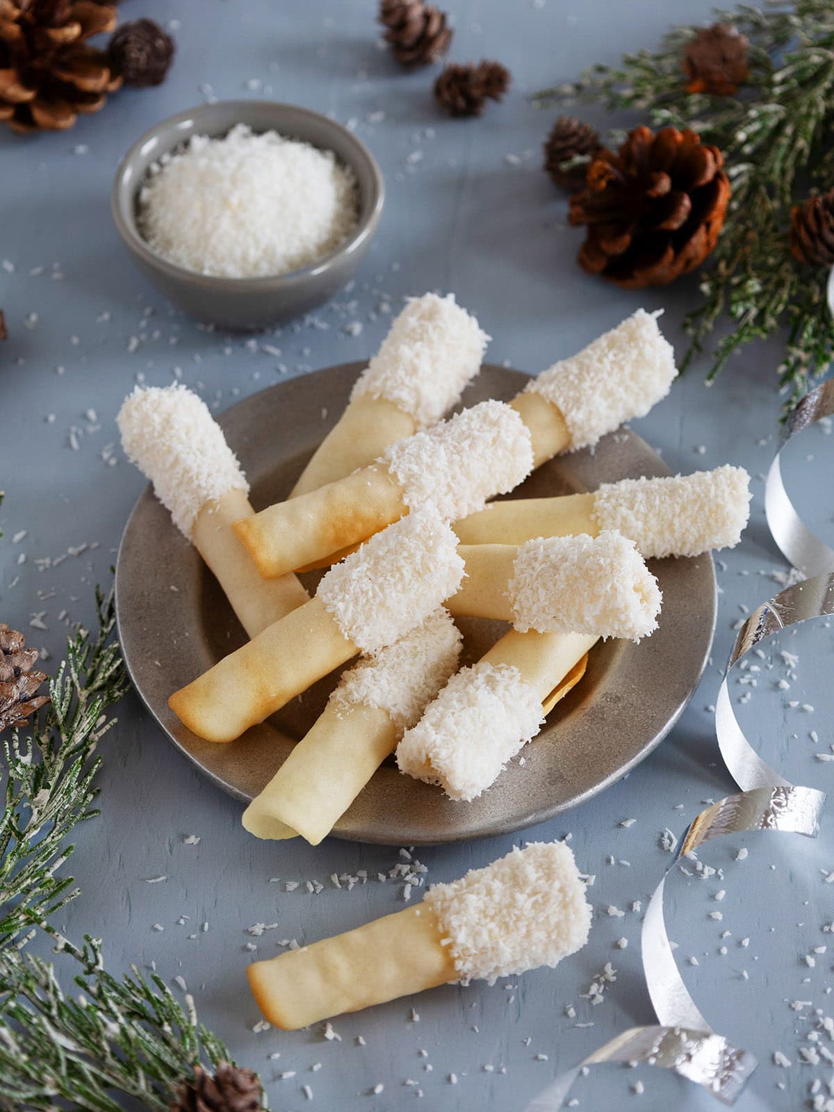 A plate of coconut pirouettes next to holiday decorations.