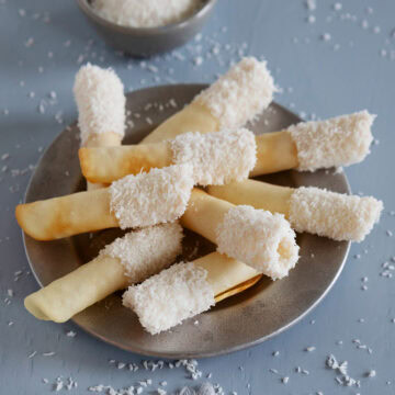 A plate of coconut pirouette cookies on a silver plate