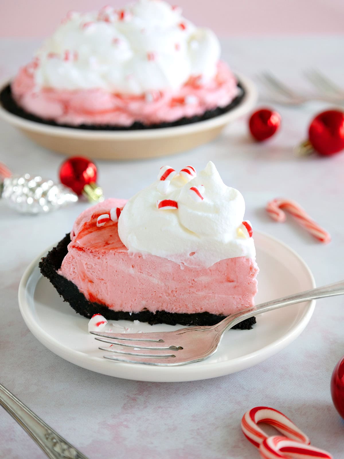A slice of peppermint pie on a dessert plate with the rest of the pie in the background.