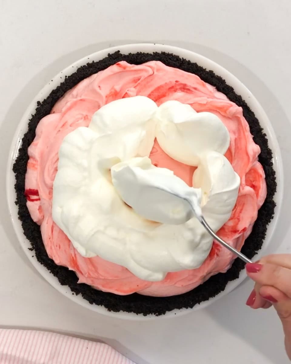Spooning whipped cream on top of a peppermint pie.