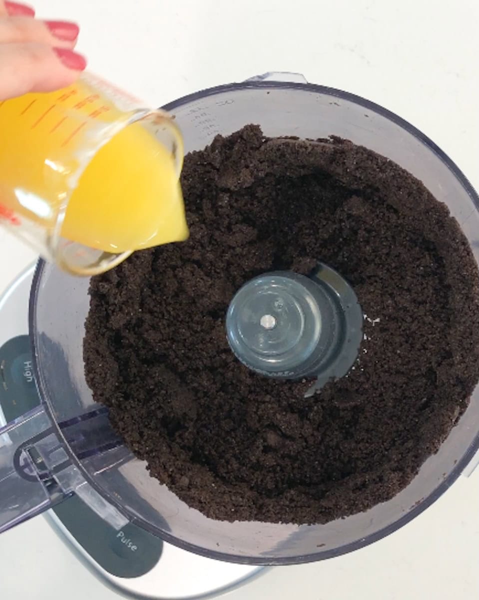Pouring butter into a food processor filled with crushed Oreos.