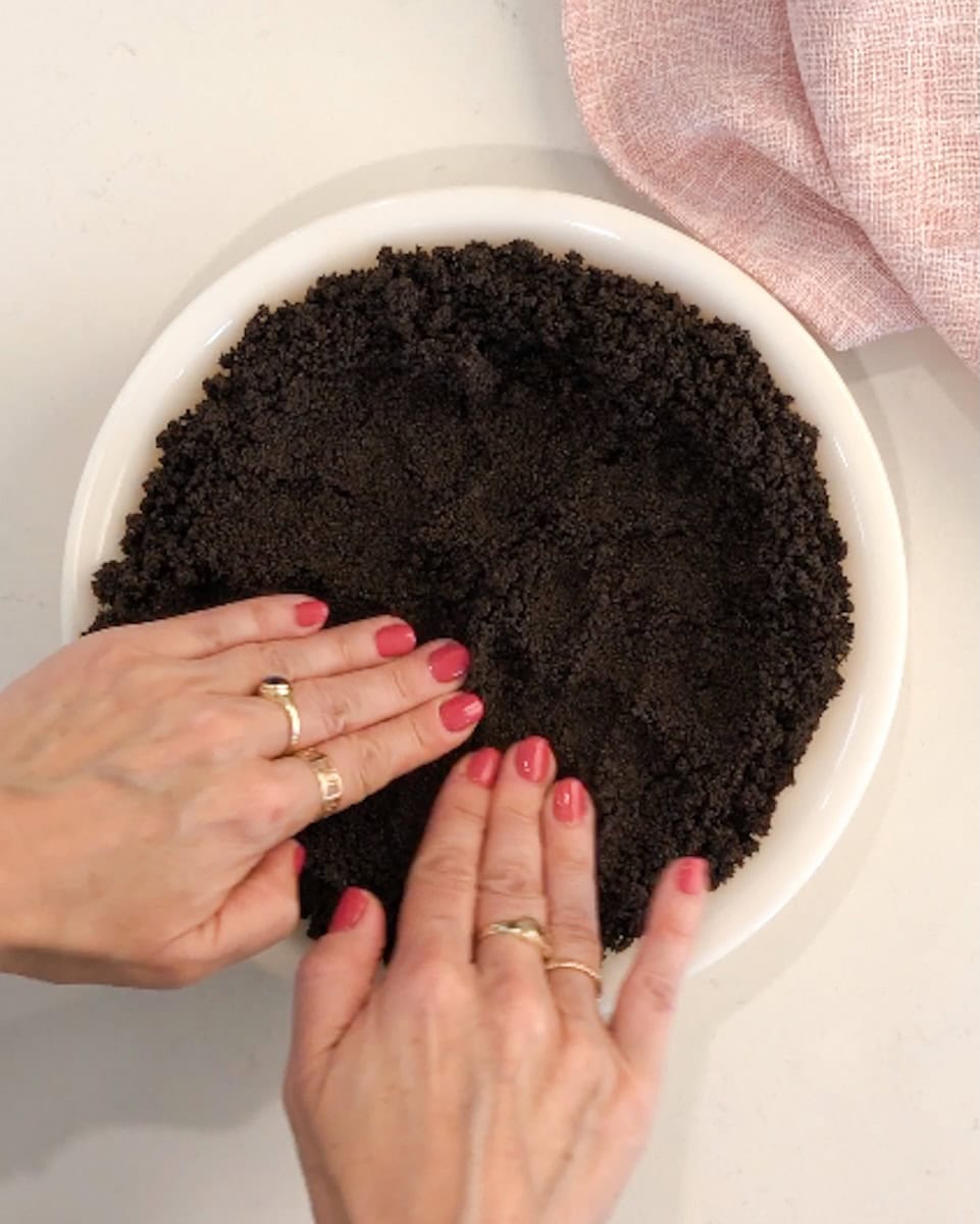 Hands pressing chocolate cookie crust into a pie pan.
