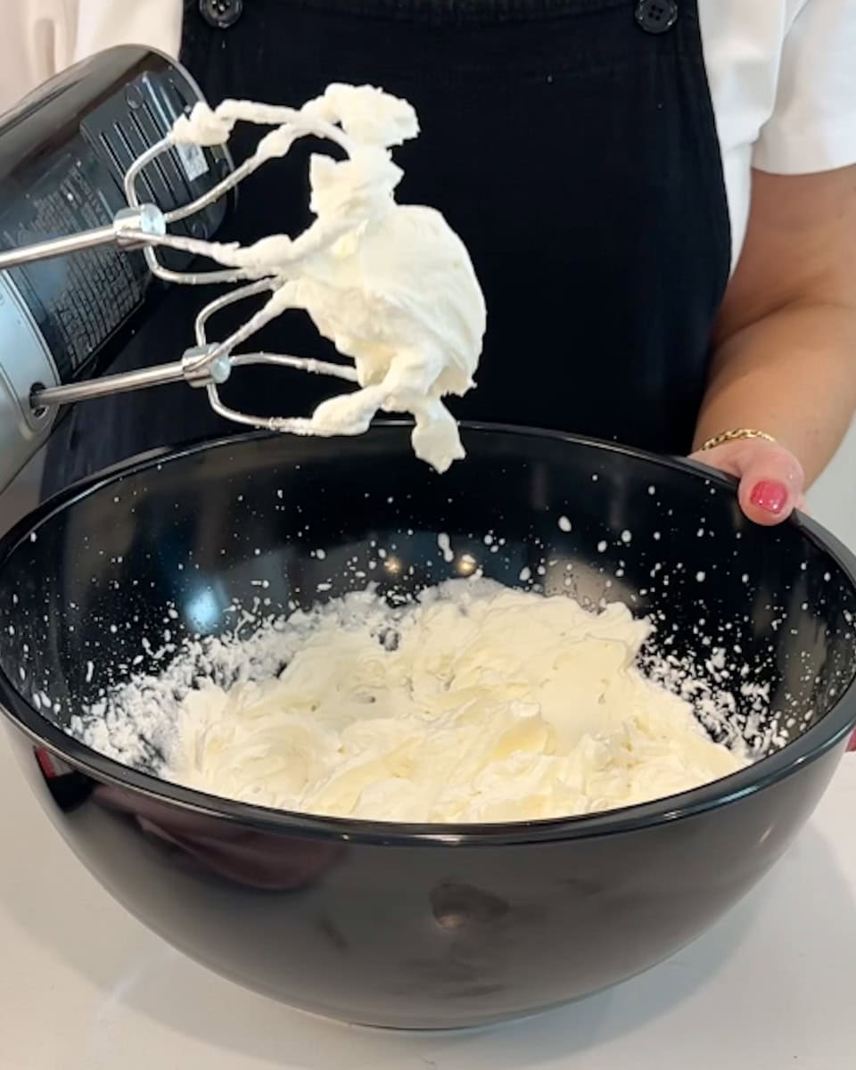 Beaters over a bowl of whipped cream showing firm peaks.